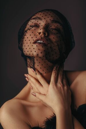 fashion portrait of beauty elegant girl posing in black veil on dark background. gorgeous stylish model woman in black dress with feathers. passion. Art creative concept of black swan or dark angelの写真素材