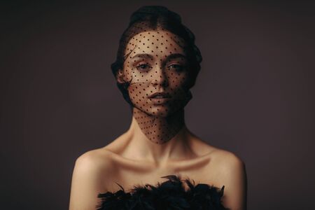 fashion portrait of beauty elegant girl posing in black veil on dark background. gorgeous stylish model woman in black dress with feathers. Art creative concept of black swan or dark angelの写真素材