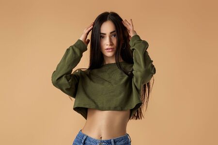 gorgeous young brunette woman model with long hair in green sweatshirt posing on beige background. fashion conceptの写真素材