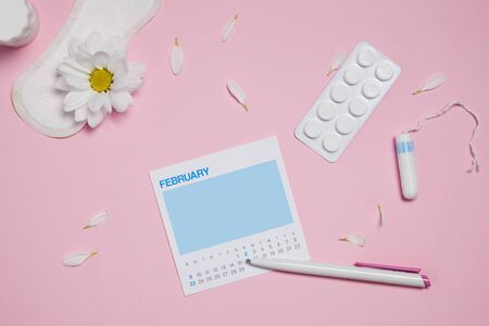 menstrual sanitary tampon, pad, pain pills during menstruation and white chamomile flower on pink background, feminine calendar with copy space. Feminine hygiene products. top view. mock upの写真素材