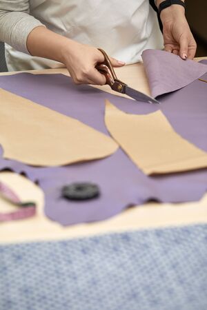 Workplace of seamstress. Dressmaker cuts textile on the sketch lines. female hand with the scissors...