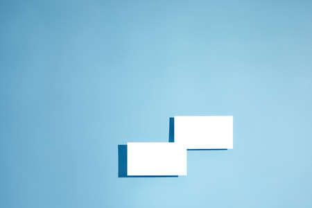 two white empty blank business cards mockup on blue background. top viewの写真素材