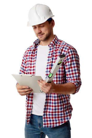 handyman worker in hard hat reads details of an order. builder in shirt with builder level and clipboard isolated on white studio backgroundの写真素材
