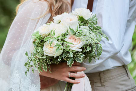 Elegant bride and groom are holding white wedding flowers bouquet outdoorの写真素材