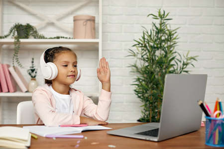 happy little child girl using laptop for studying online. child raises her hand to answer the teachers question. online education conceptの写真素材