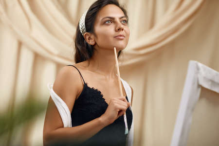 portrait of young happy woman with brush painting in art studio. smiling female artist in front of easel.の写真素材