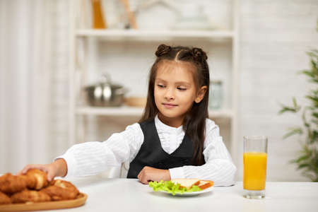 happy little child girl in school uniform having breakfast - sandwich and orange juice in the kitchen. healthy breakfastの写真素材