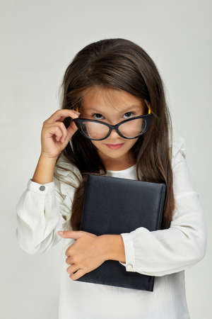 cute little child girl in glasses holding notebook and looking at the camera on white background.の写真素材