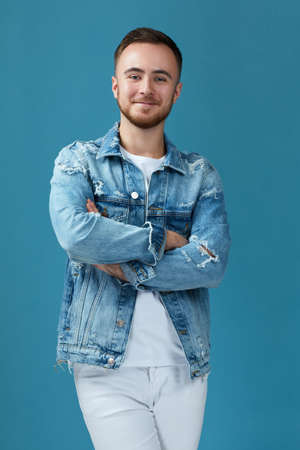 handsome smiling man in denim with crossed arms looking at camera isolated on blue studio background