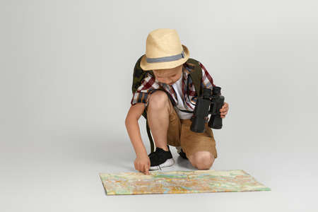 Little boy tourist with backpack holding binoculars and map. child is looking on the map. Little boy...