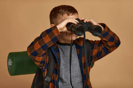 Little boy tourist with backpack looking through a binoculars. Little boy scout dreams of traveling