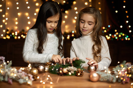 two cute little child girls make a handmade Christmas wreath at home. Merry Christmas and Happy Holidaysの写真素材