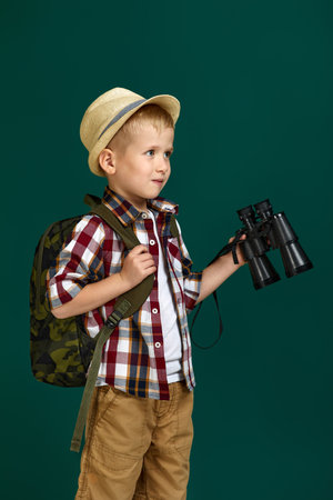 Little boy tourist with backpack holding binoculars. Little boy scout dreams of travelingの写真素材