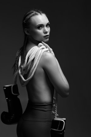 fashion sexy gorgeous woman model with black boxing gloves and white rope on studio background. portrait of glamour female boxer looking at the camera. black and whiteの写真素材
