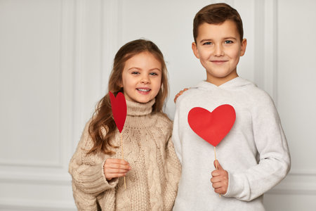 Happy couple little girl and boy with red hearts against white wall. smiling boy hugs girl. St. Valentines Dayの写真素材