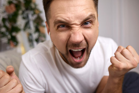 angry young man in earphones is talking to somebody on video call. man yellingの写真素材