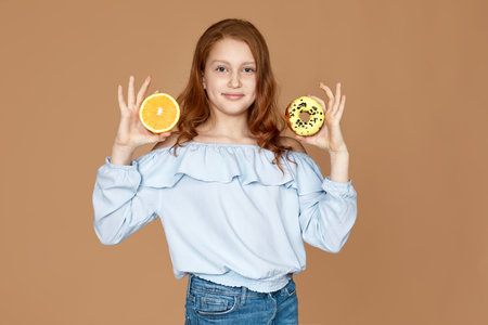 child girl holding yummy chocolate donut and fresh orange isolated on studio background.