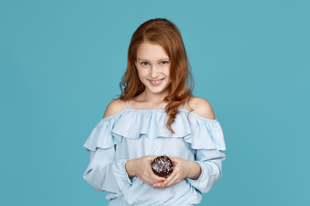 smiling child girl holding in hand cake isolated over blue background