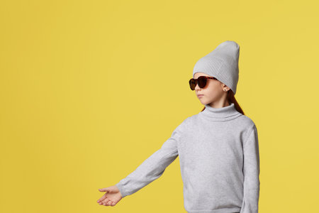 Stylish little child girl in hat pointing to empty place on yellow background. copy spaceの写真素材
