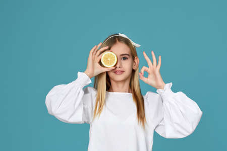 adorable little child girl holding fresh juicy lemon and showing Ok gesture isolated over blue backgroundの写真素材