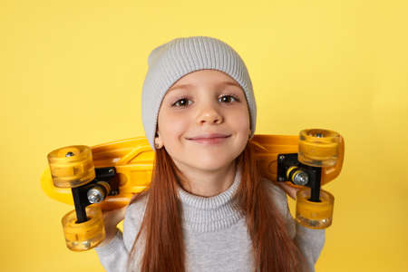 happy little child girl in hat with yellow skateboard having fun over yellow backgroundの写真素材