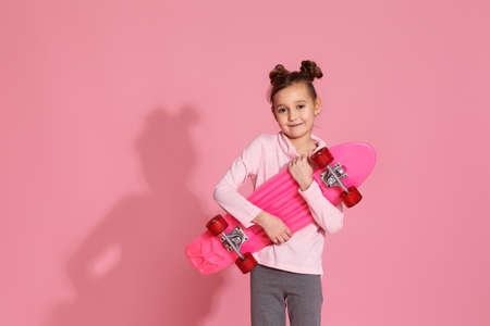 adorable little child girl with pink skateboard in casual clothes on pink background.