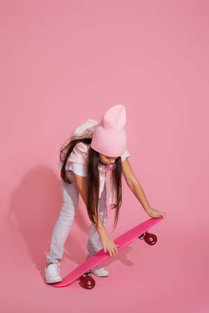 little child girl with pink skateboard in casual clothes on pink studio background.の写真素材
