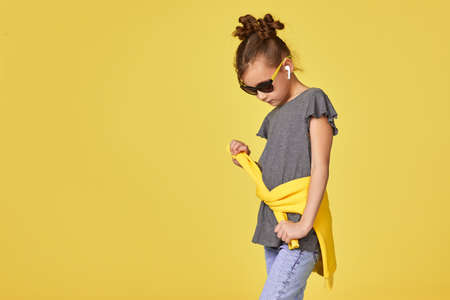 fashionable little child girl in sunglasses posing on yellow studio background. copy spaceの写真素材