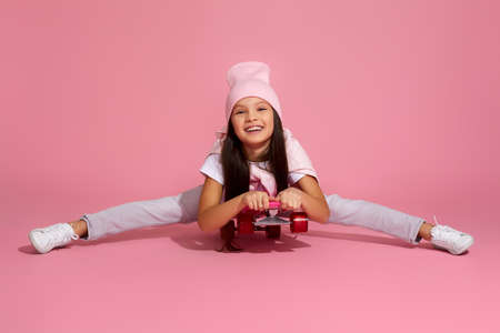 happy little child girl riding on skateboard over pink background. kid having fun