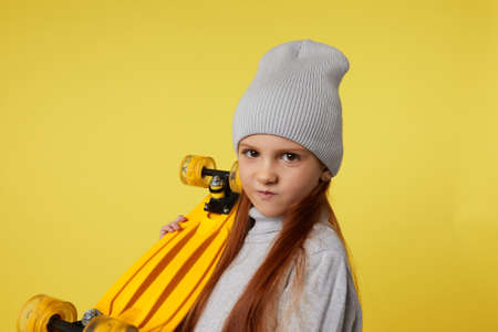 little child girl in hat with yellow skateboard over yellow backgroundの写真素材