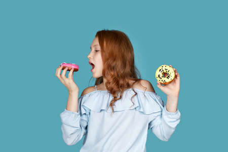 cute child girl is eating yummy donut isolated over blue background