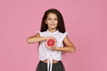 adorable little child girl holding fresh juicy grapefruit isolated on pink background