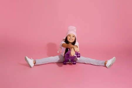 happy cute little child girl on skateboard having fun over pink background.の写真素材