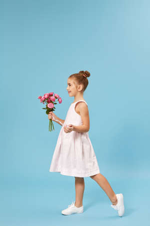 beautiful smiling little girl holding bouquet of roses isolated on blue studio background. side viewの写真素材