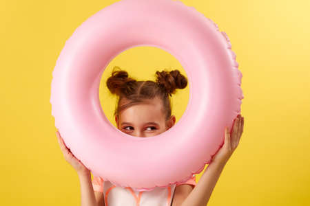 little child girl in swimwear with pink inflatable rubber ring on yellow background