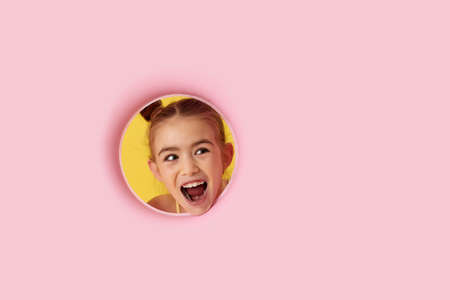 super excited little child girl looking aside through the hole on pink backgroundの写真素材