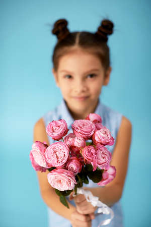 smiling little girl showing bouquet of pink roses on blue background. focus on flower