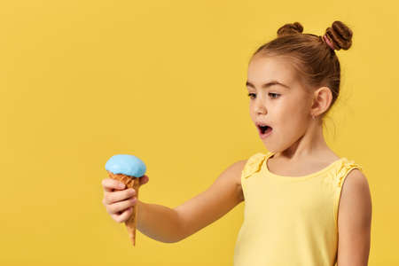 very excited little girl with ice cream in a waffle cone on yellow background.の写真素材