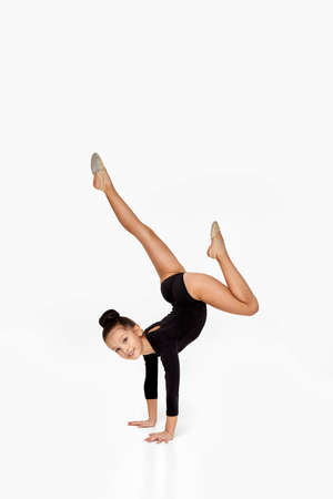 adorable little gymnast girl in black sportswear performs a handstand. child showing flexibility and acrobat balanceの写真素材