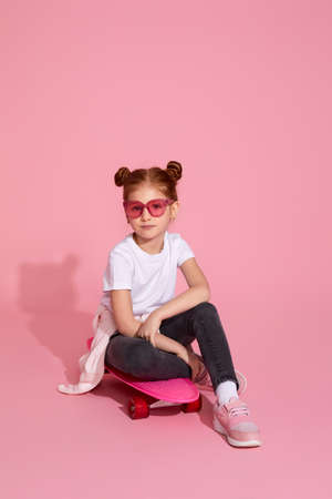 cute redhead little child girl sitting on skateboard, wearing pink sunglassesの写真素材