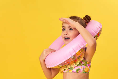 little child girl with inflatable rubber ring looks into the distance on yellow background. copy spaceの写真素材
