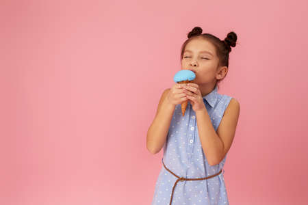 smiling little girl eating ice cream in a waffle cone on pink background. copy spaceの写真素材