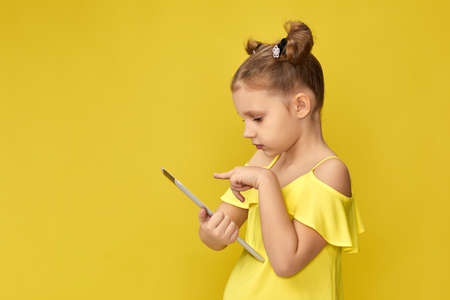 funny little child girl in yellow t-shirt using digital tablet on yellow backgroundの写真素材