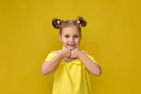 funny little child girl having fun on yellow studio background. kid holding finger on lips