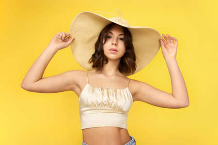 beautiful tanned young woman in summer hat on yellow background.の写真素材