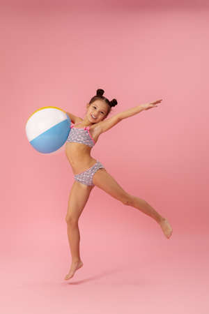 funny little child girl in swimsuit with beach ball jumping on pink backgroundの写真素材