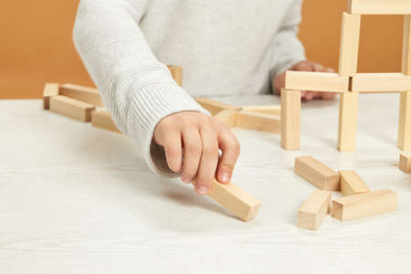 children plays with wooden constructor on desk.