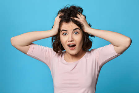 scared curly young brunette woman on blue background.の写真素材