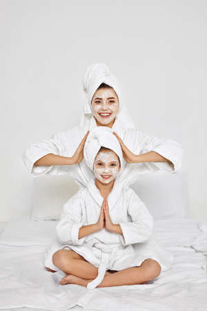 mother and daughter are sitting with towels on head and facial mask.の写真素材