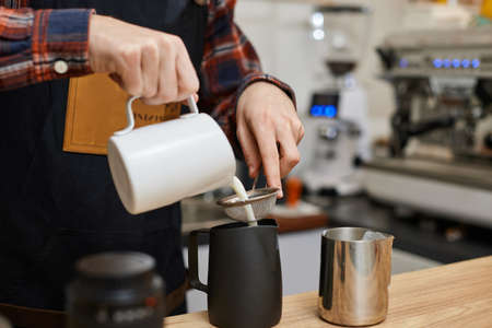 Caucasian man pouring hot milk in coffee.の写真素材